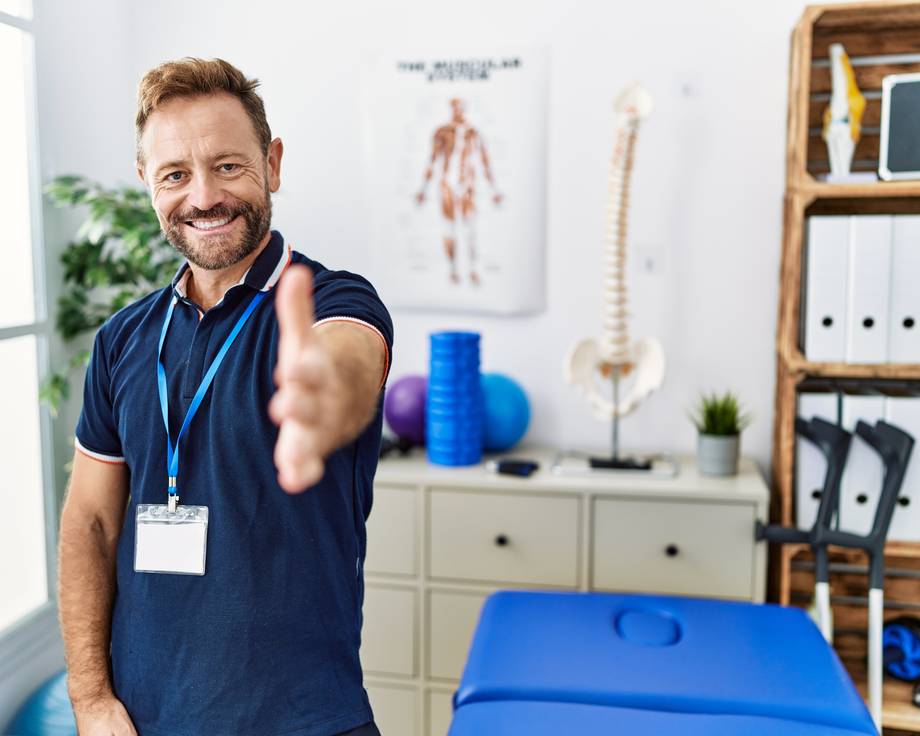 Mittelalter Physiotherapeut Mann lächelt freundlich und bietet Händedruck als Begrüßung an