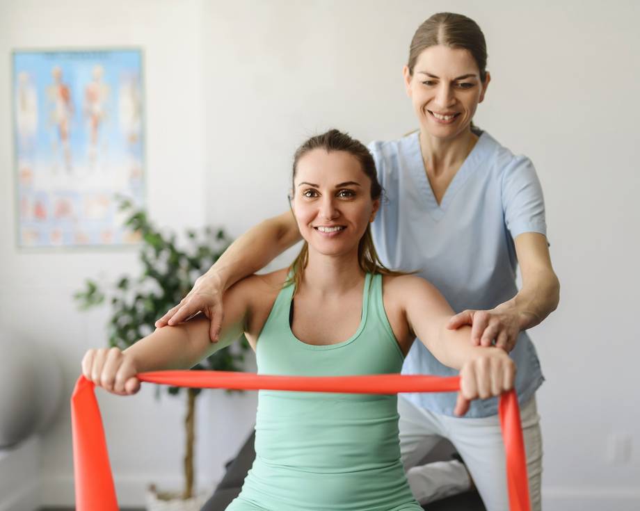 Rehabilitation: Physiotherapeutin und Patientin arbeiten mit elastischem Band