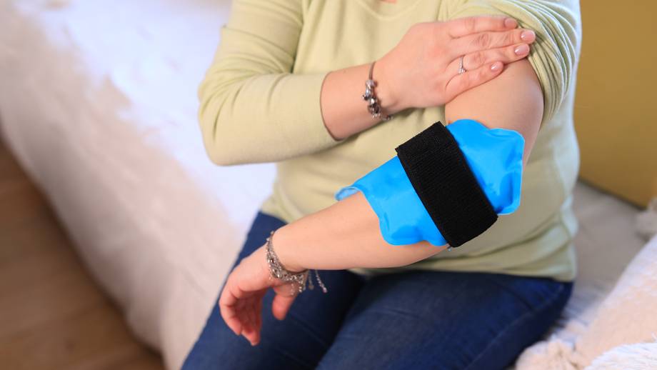 Frau mit Ellbogen- und Armschmerzen verwendet kaltes Eispack-Gel.