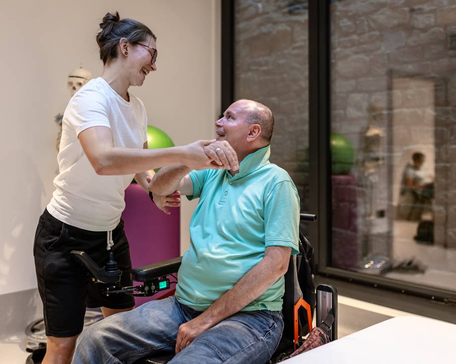 Eine behinderte Person im Rollstuhl mit einem Physiotherapeuten, der seinen Arm leicht anhebt