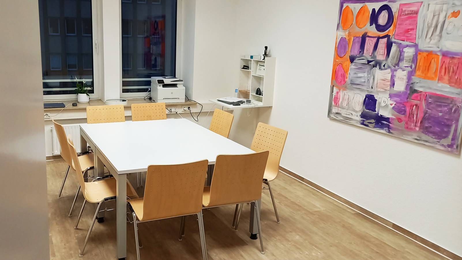 Ein privates Besprechungszimmer mit einem Tisch und Stühlen, einem Fenster und einem abstrakten Gemälde an der Wand.