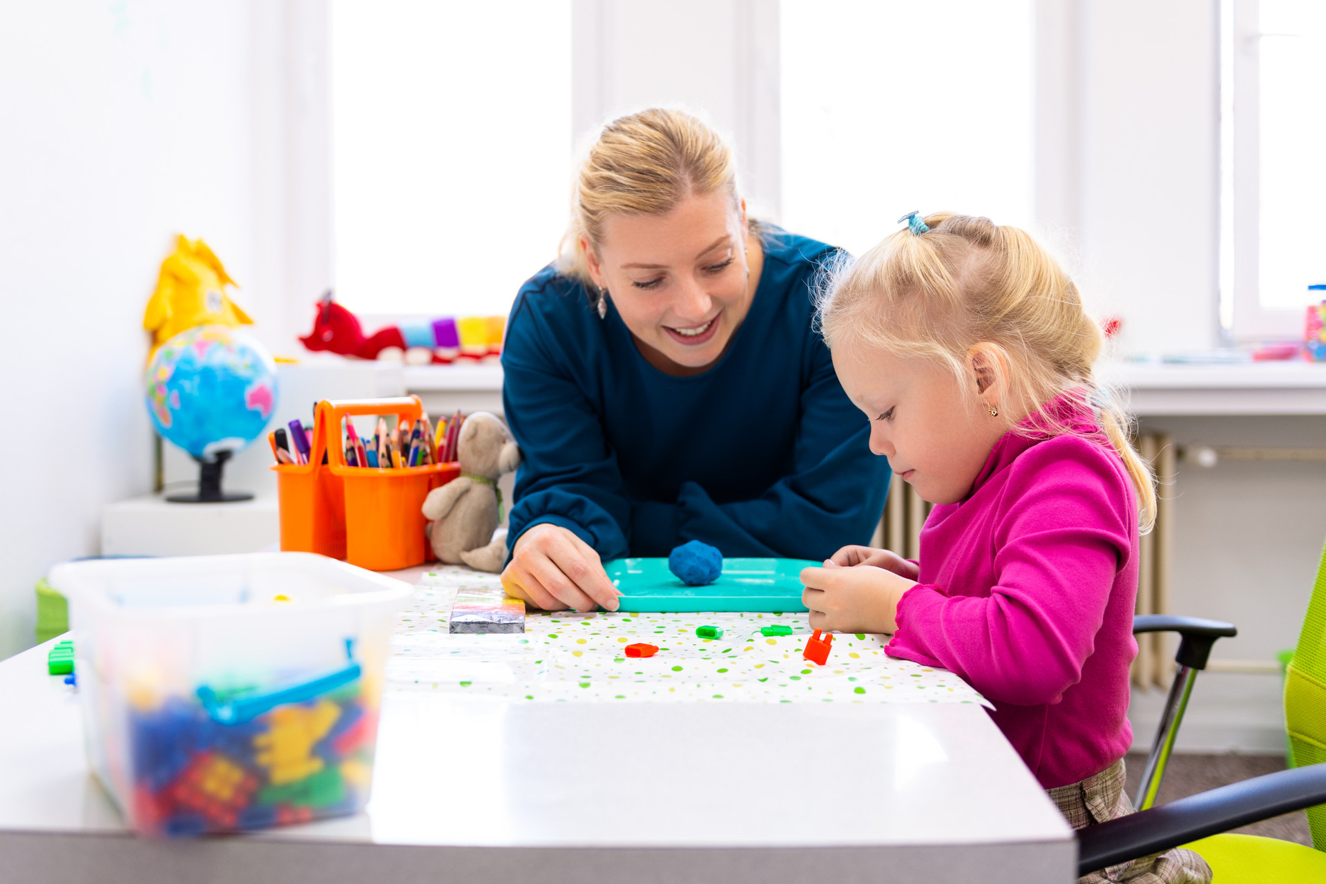 Frau mit blondem Mädchen Junges Mädchen führt konzentriert ihre spielerische, sensorische Übung mit ihrer Therapeutin beim Basteln durch.