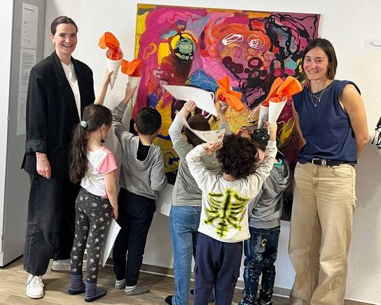 Eine Gruppe von Erwachsenen und Kindern steht vor einem großen, farbenfrohen Gemälde in einer Galerie.
