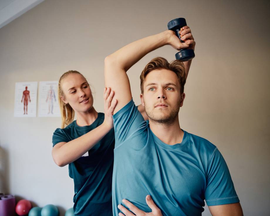 Junge Physiotherapeutin hilft Patienten, Hanteln zu heben