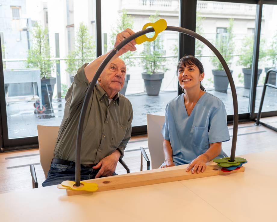 Älterer männlicher Patient, der in der Ergotherapie mit einer Therapeutin Teile von einer Seite zur anderen bewegt